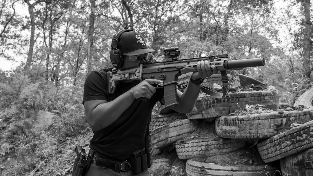 a-man-holding-a-rifle-while-standing-next-to-a-pile-of-barrels-ujbsyrz5xum